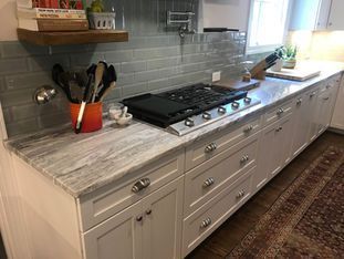A kitchen with white cabinets , granite counter tops , and a stove top oven.