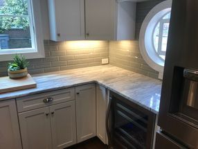 A kitchen with white cabinets , stainless steel appliances , granite counter tops and a round window.