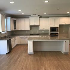 A kitchen with white cabinets , granite counter tops , stainless steel appliances and hardwood floors.