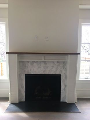 An empty living room with a fireplace and two windows.