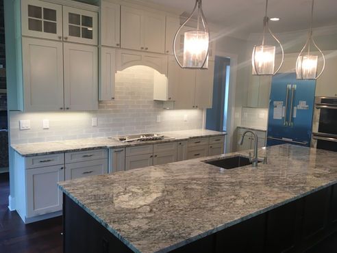 A kitchen with granite counter tops , white cabinets , a sink and a refrigerator.