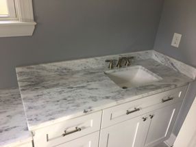 A bathroom sink with a marble counter top and white cabinets.