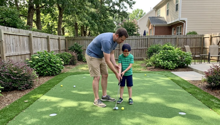 A father and son smiling while playing golf on a beautiful backyard putting green in Raleigh, NC.