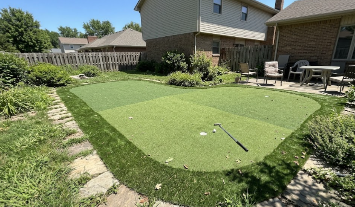 A custom designed residential putting green with dark green fringe next to a patio in a home backyard.