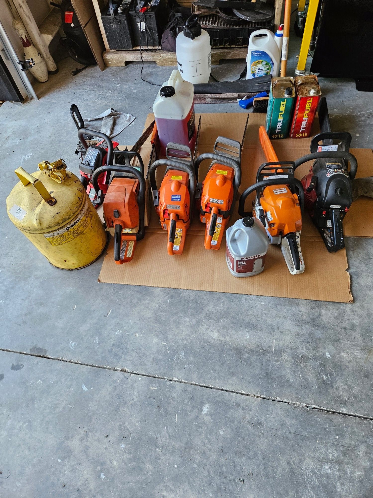 A group of chainsaws sitting on top of a cardboard box in a garage.