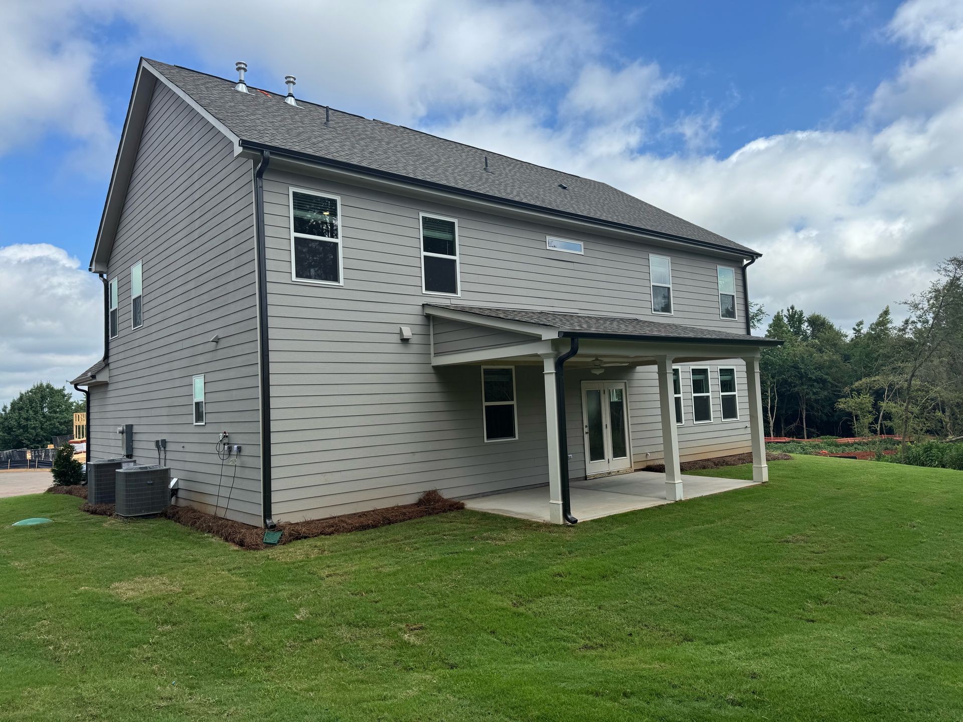 A large house with a covered porch and a lot of windows is sitting on top of a lush green field.