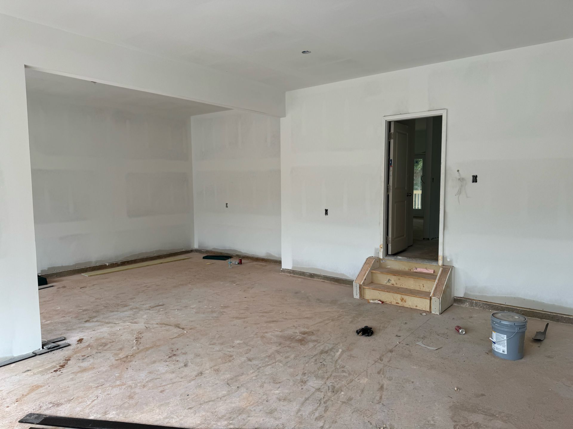 An empty room with white walls and a bucket on the floor.