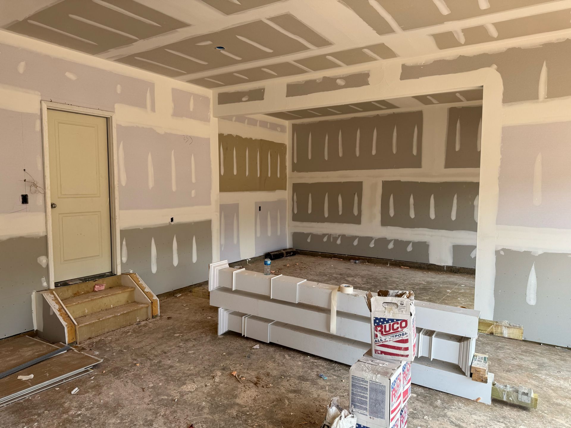 A room with a lot of drywall on the walls and a door.