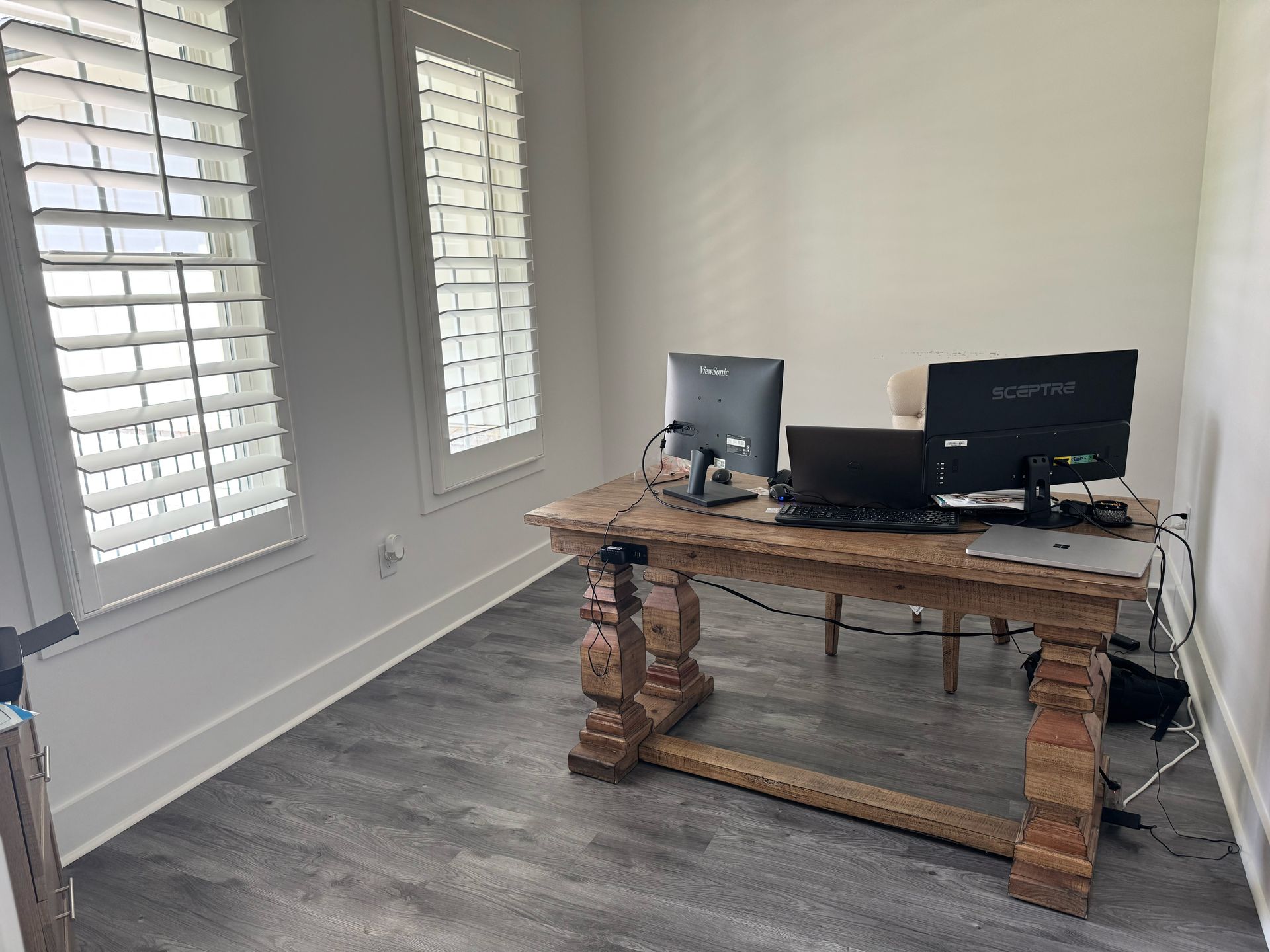 A wooden desk with two computer monitors on it in a room with shutters.