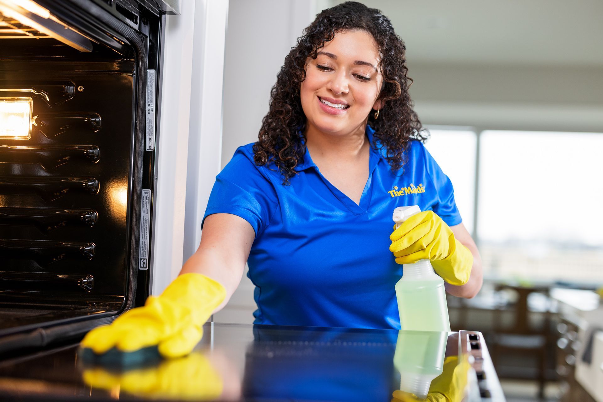 A woman in a blue shirt and yellow gloves is cleaning an oven.