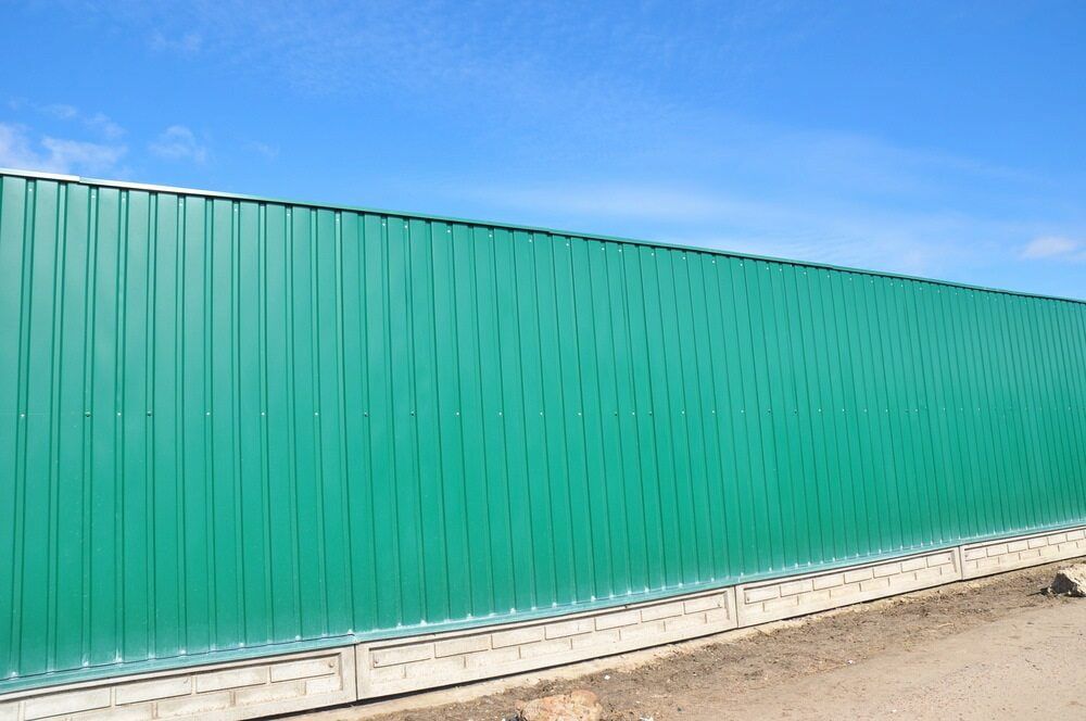 Green corrugated metal fence against a blue sky. — CAW Services in Badagarang, NSW