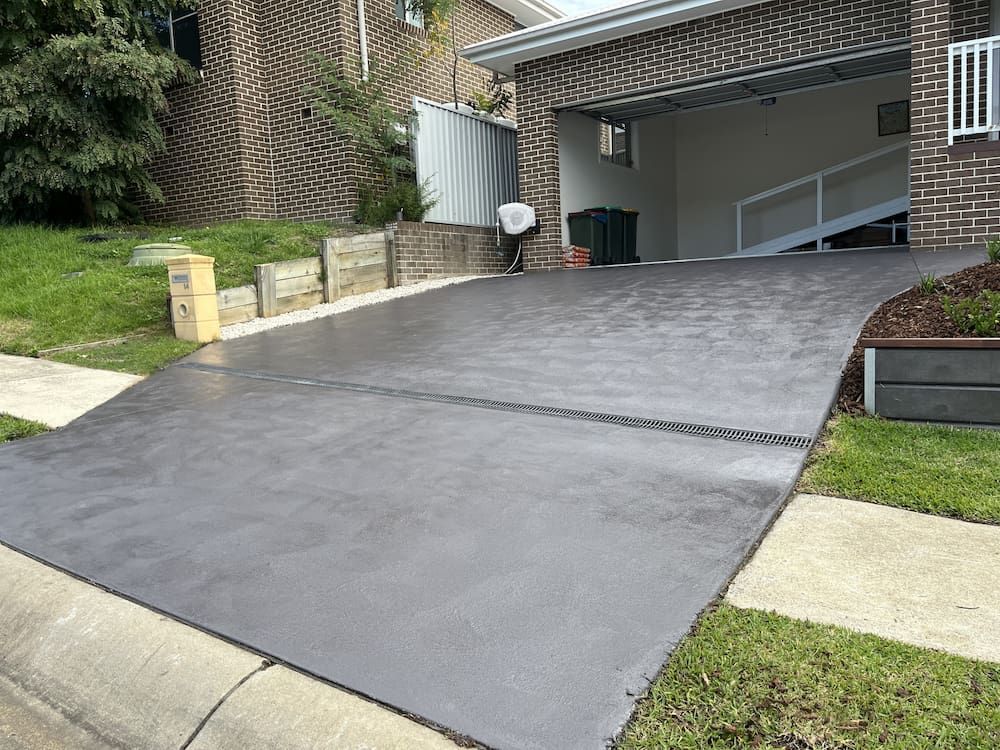 Newly Paved Dark Gray Concrete Driveway Leading to a Garage — CAW Services in Badagarang, NSW