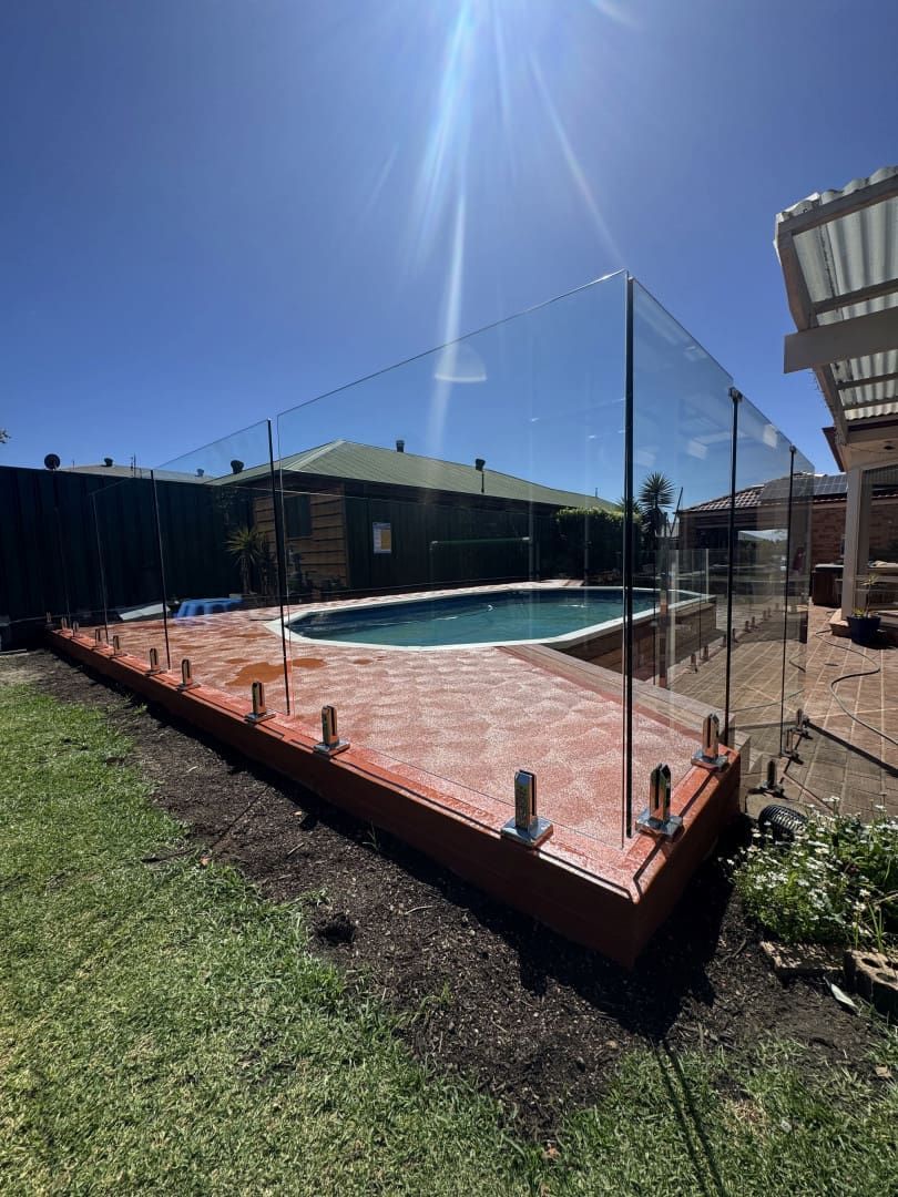 Glass Pool Fence Surrounds a Red Brick Patio With a Pool Beyond on a Sunny Day — CAW Services in Badagarang, NSW