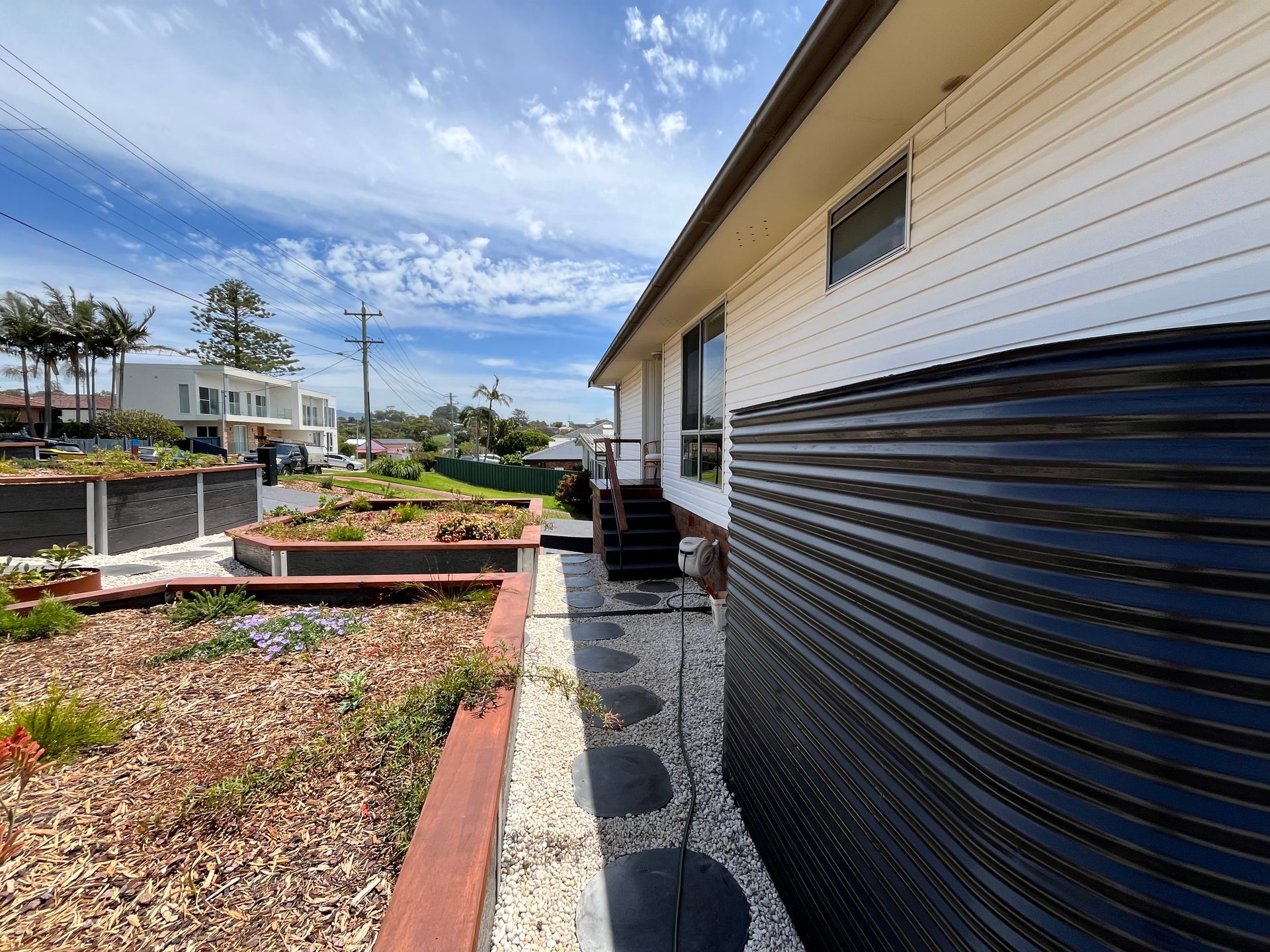 Side view of a house with white siding and a black corrugated storage unit. A garden bed is in front  — CAW Services in Badagarang, NSW