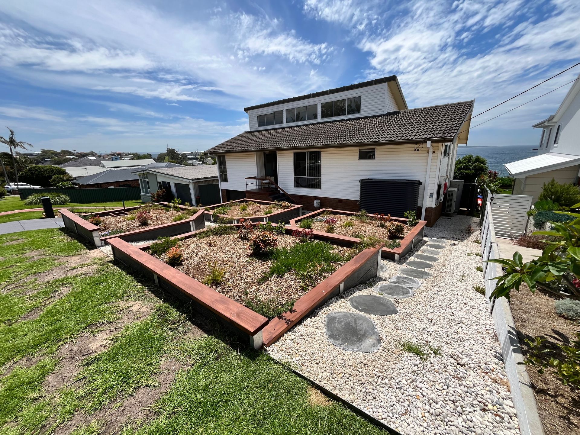 A White House With Tiered Garden Beds Along the Sidewalk — CAW Services in Badagarang, NSW