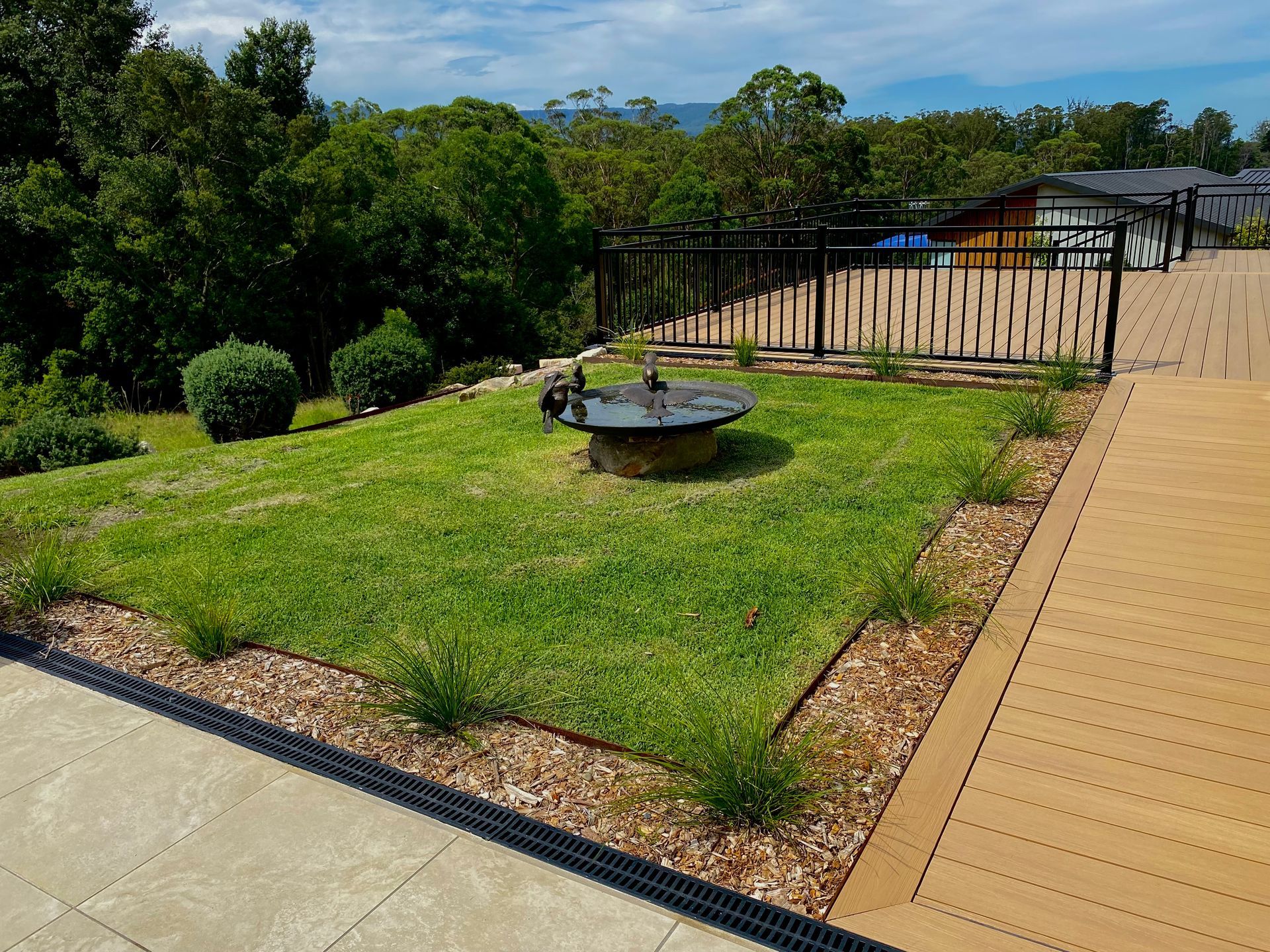 Grassy area with fire pit, bordered by wood chips and a wooden deck, overlooking a landscape. — CAW Services in Badagarang, NSW