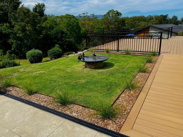 Green Lawn with A Fire Pit Bordered by Plants and A Wooden Deck — CAW Services in Badagarang, NSW