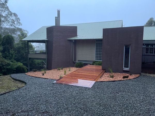 Modern House with Brown Brick Facade Wooden Walkway Over Gravel Path — CAW Services in Badagarang, NSW