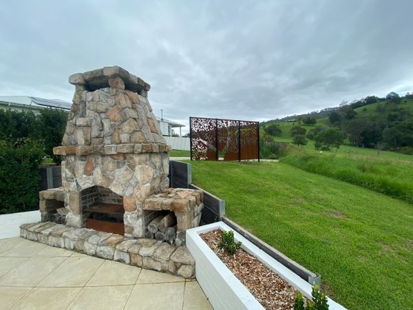 Stone Outdoor Fireplace on A Patio Overlooking a Green Lawn and Hills — CAW Services in Badagarang, NSW