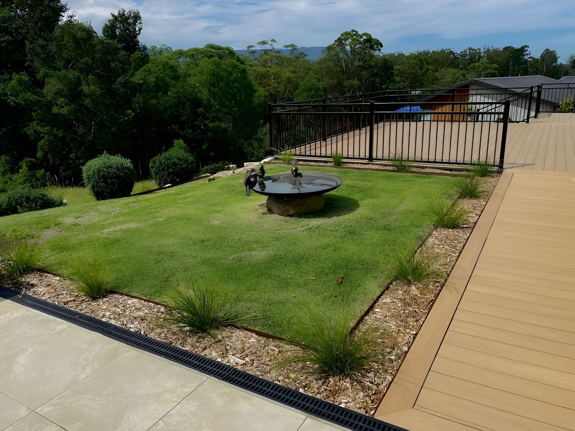 Lush Green Lawn With Fire Pit, Bordered by Plants and Wood Chips, Black Fence — CAW Services in Badagarang, NSW