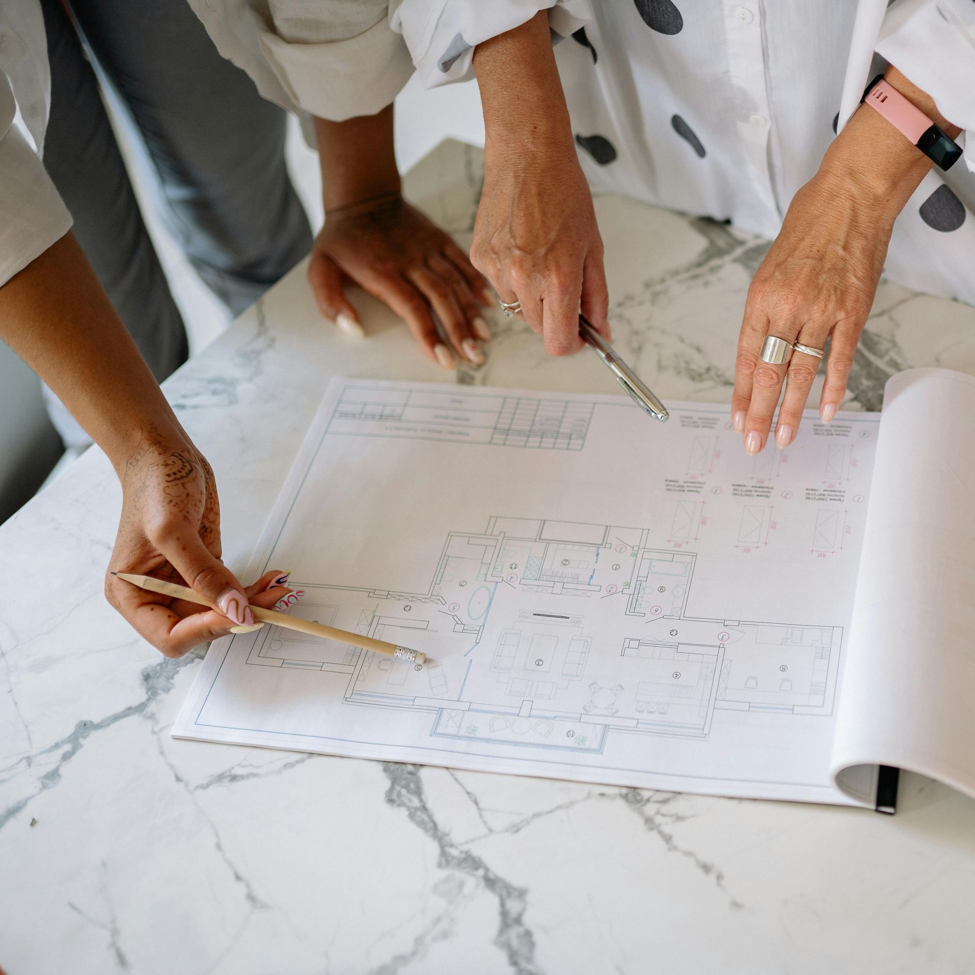Hands pointing at a blueprint on a marble surface; people discussing design.
