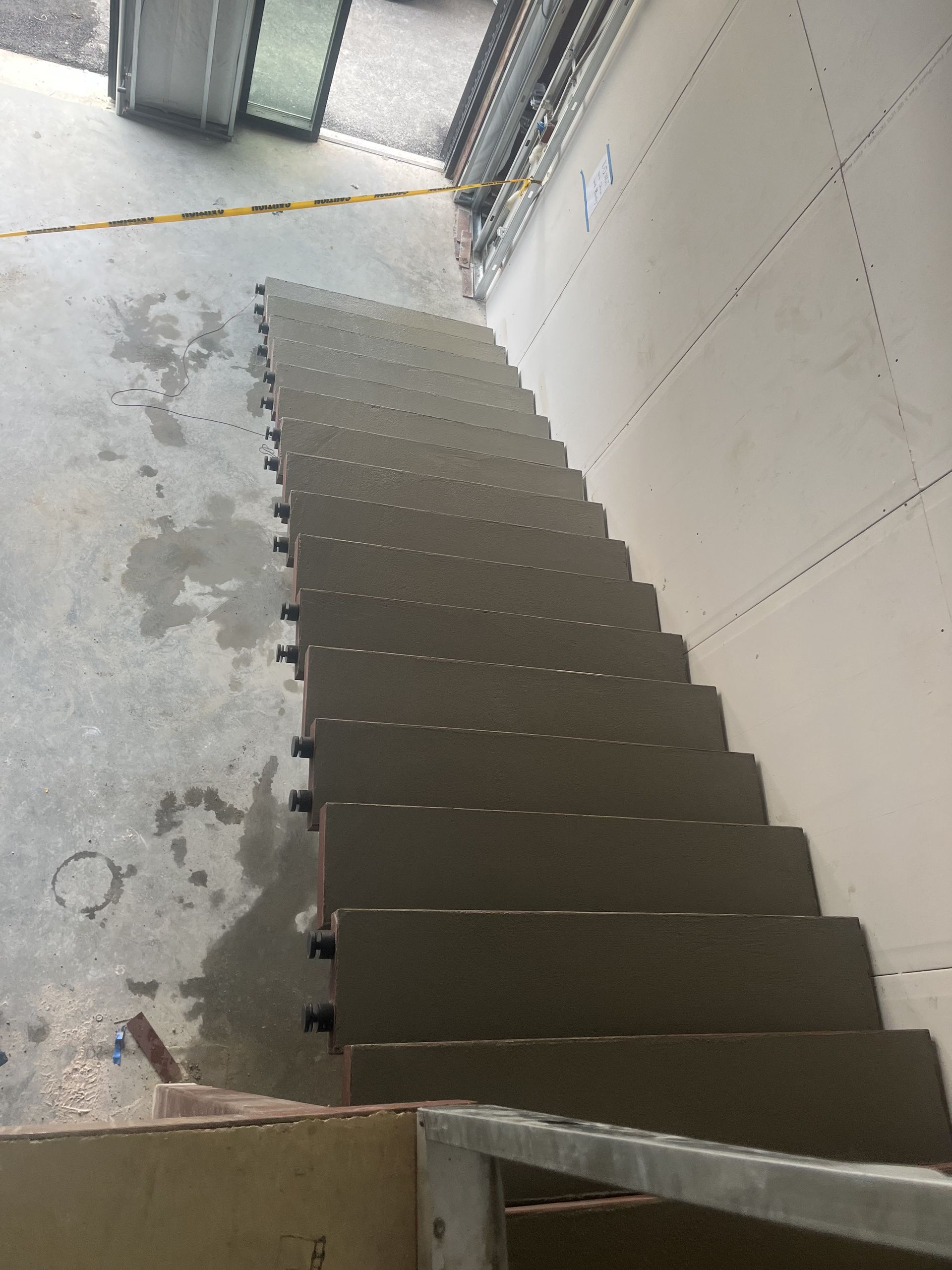 Staircase with gray steps leading up from a concrete floor, inside a structure with white walls.