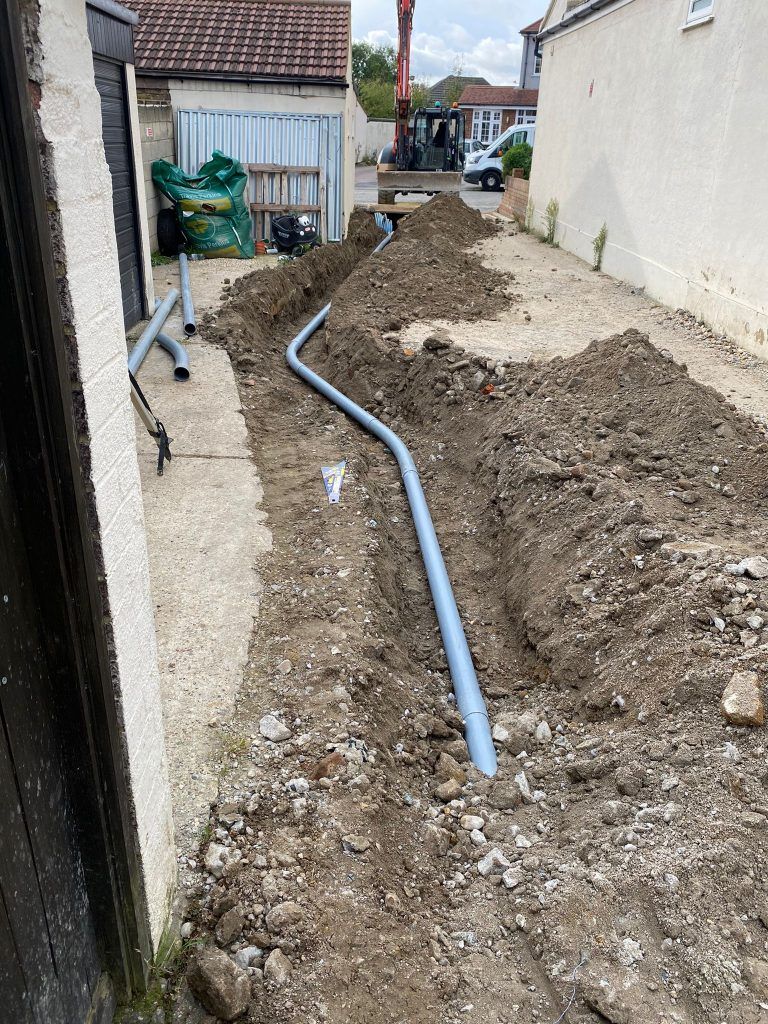 A pipe is being installed in the dirt next to a building.