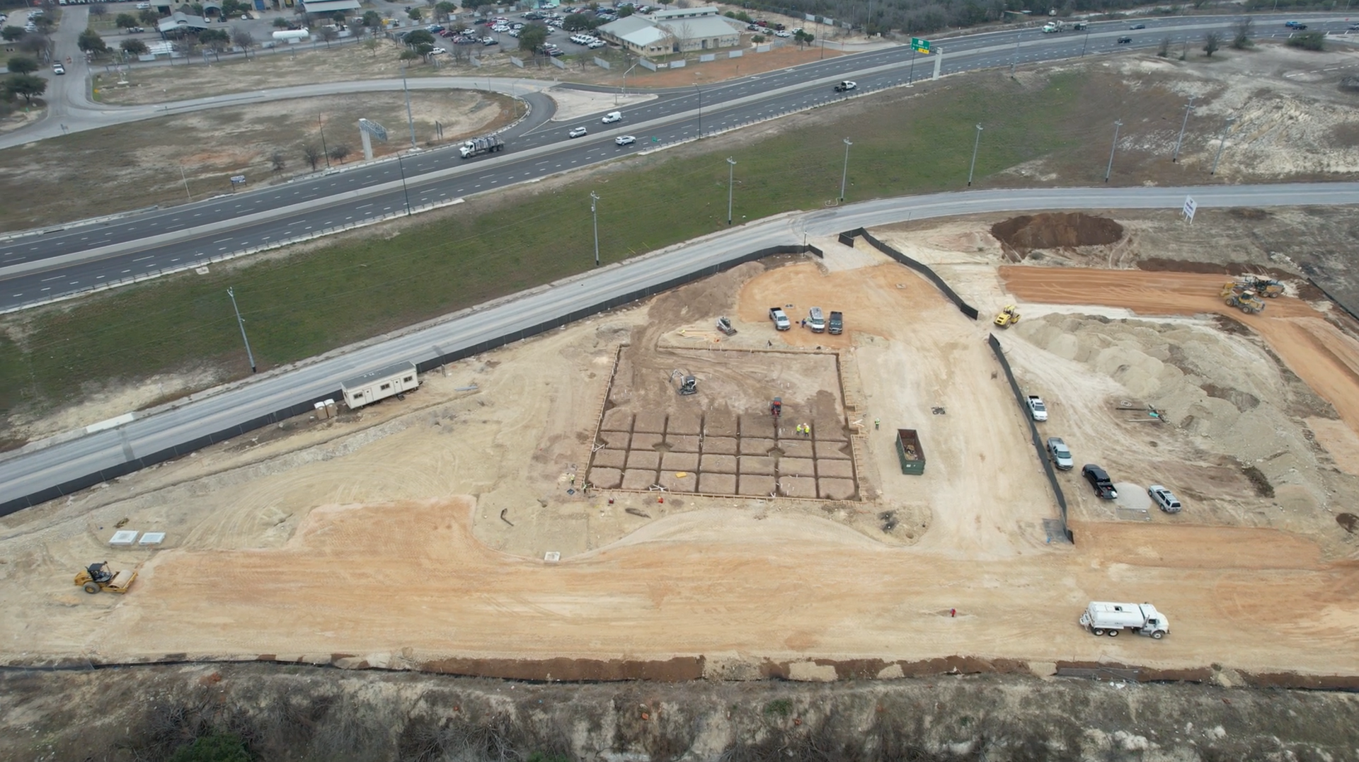 An aerial view of a construction site with a highway in the background.