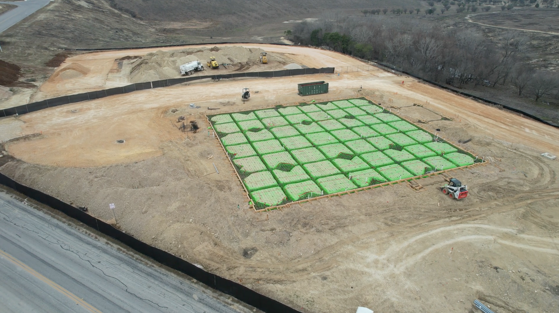 An aerial view of a construction site with a large green square in the middle.