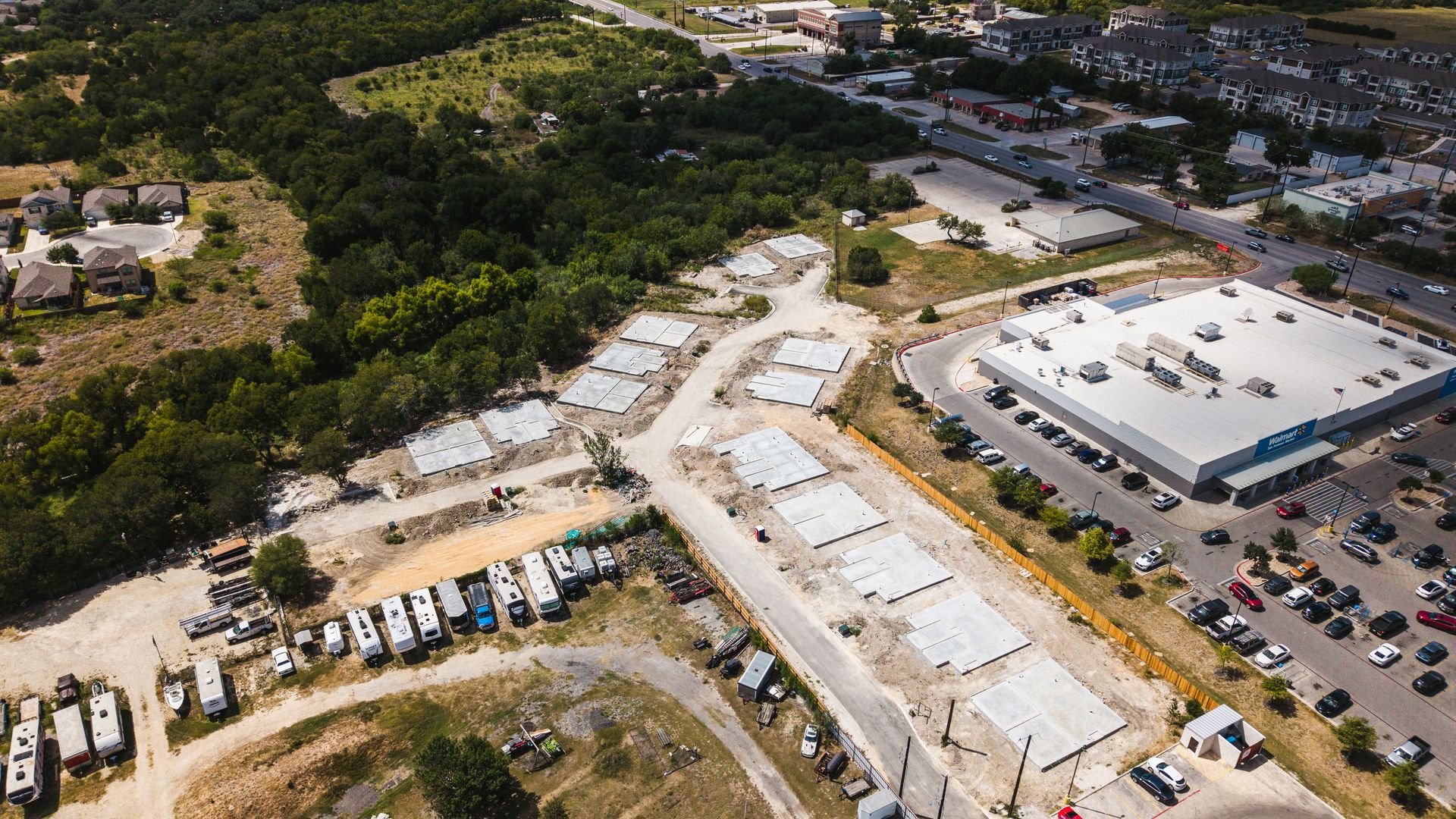 Aerial view of construction site with concrete foundations and RV parking. A large store is also visible.
