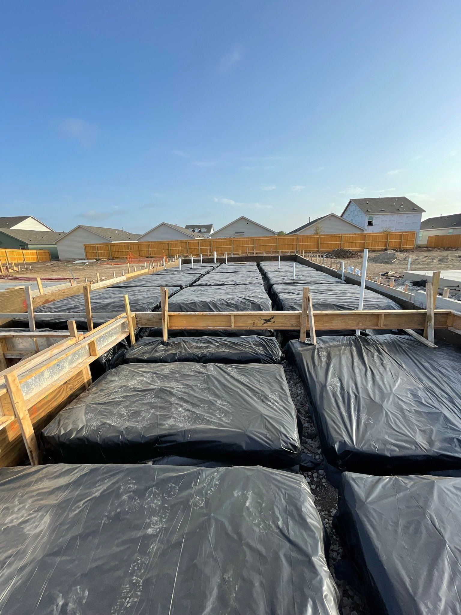 The foundation of a house is being built and covered in plastic.