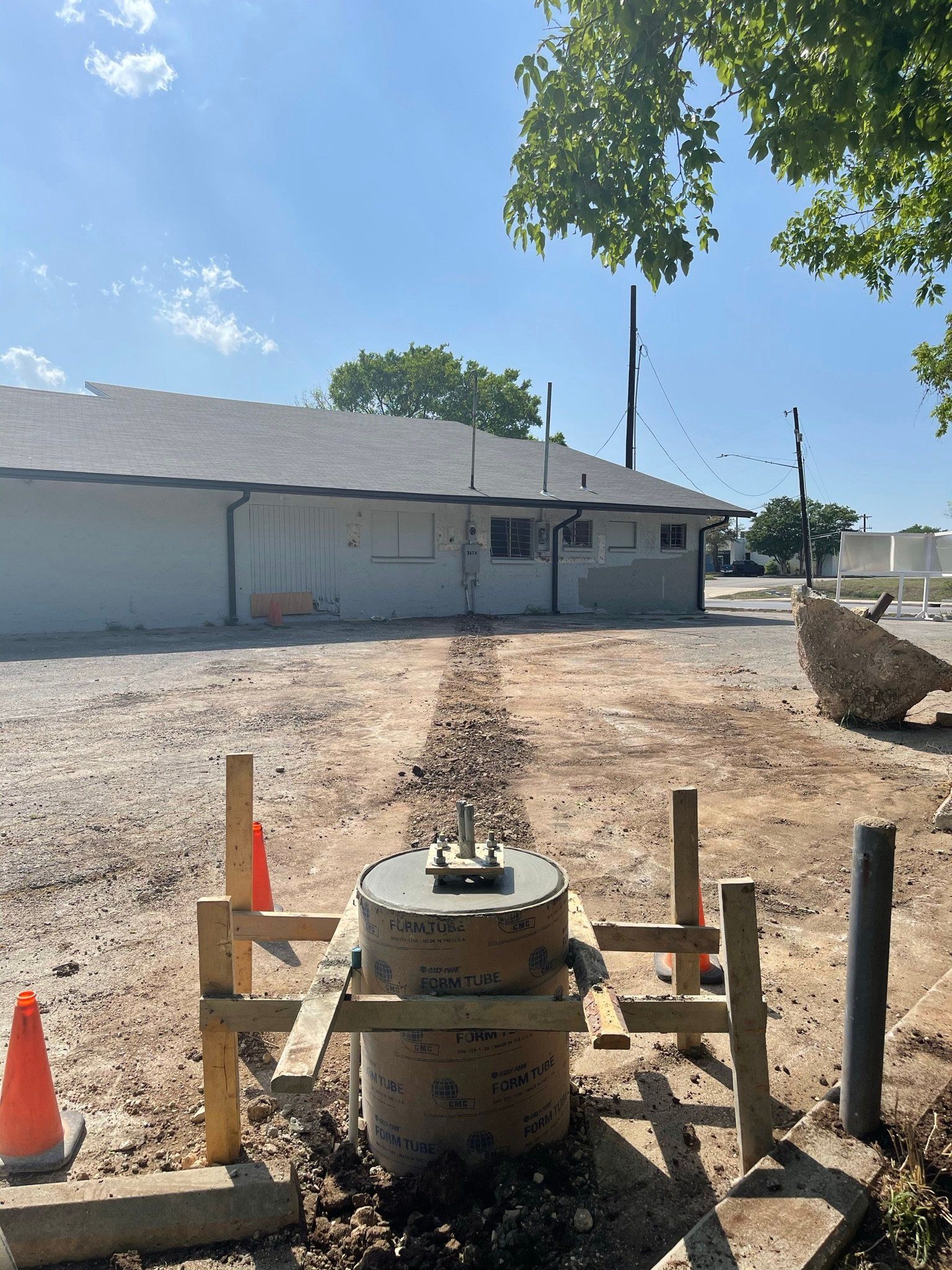 A large concrete cylinder is sitting in the dirt in front of a building.