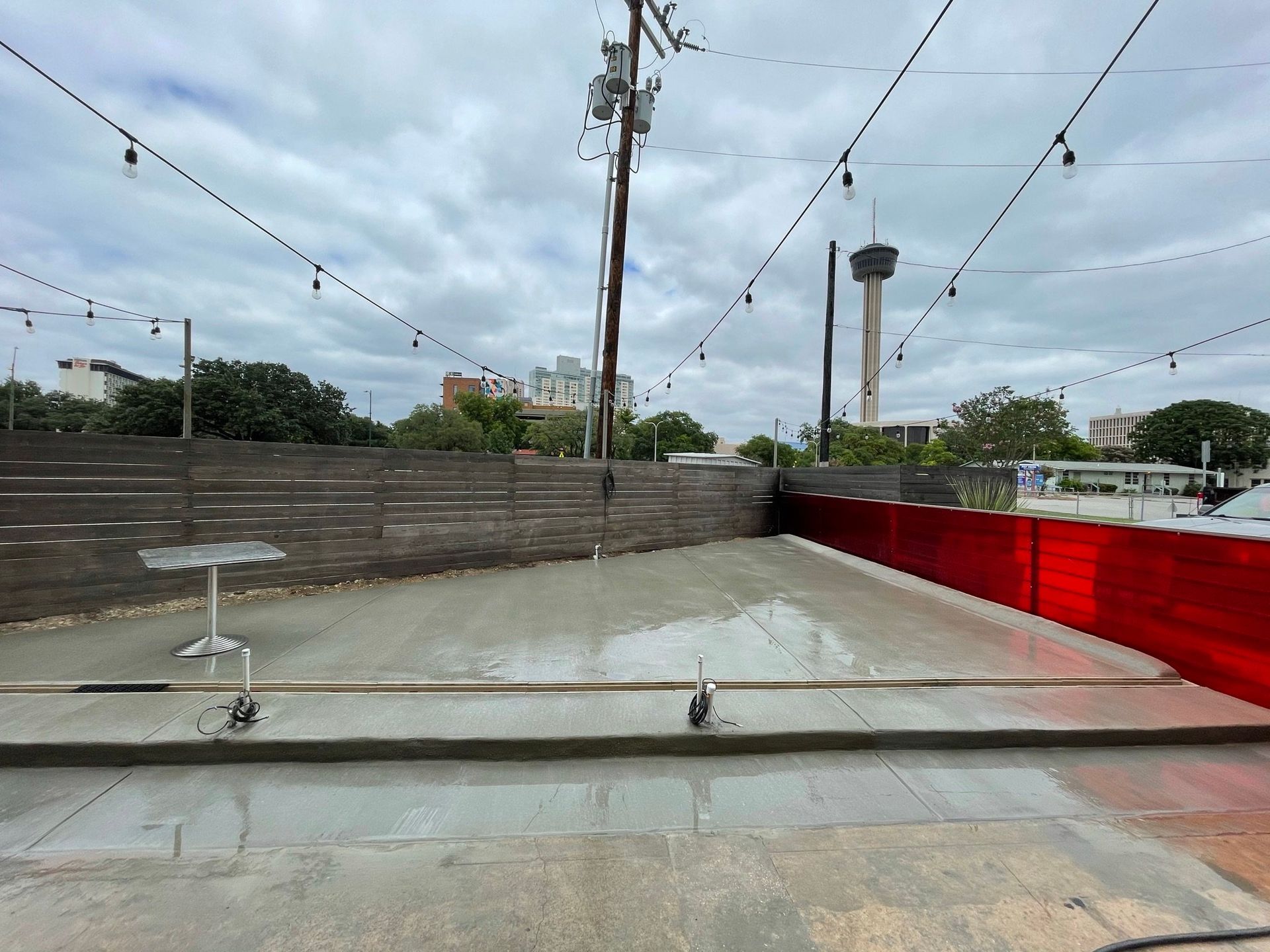 A concrete patio with a table and chairs and a red fence.