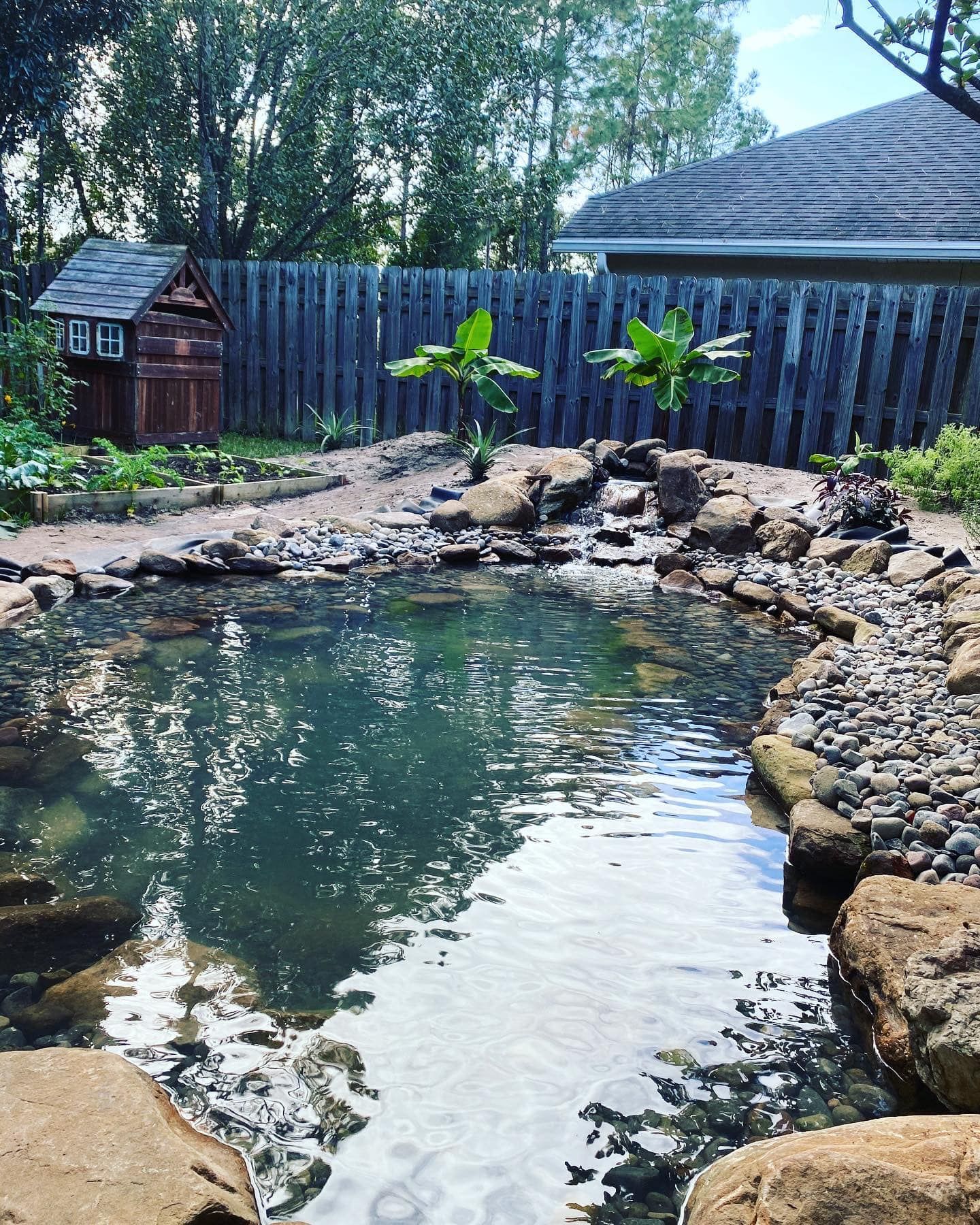 A pond surrounded by rocks and a wooden fence in a backyard.