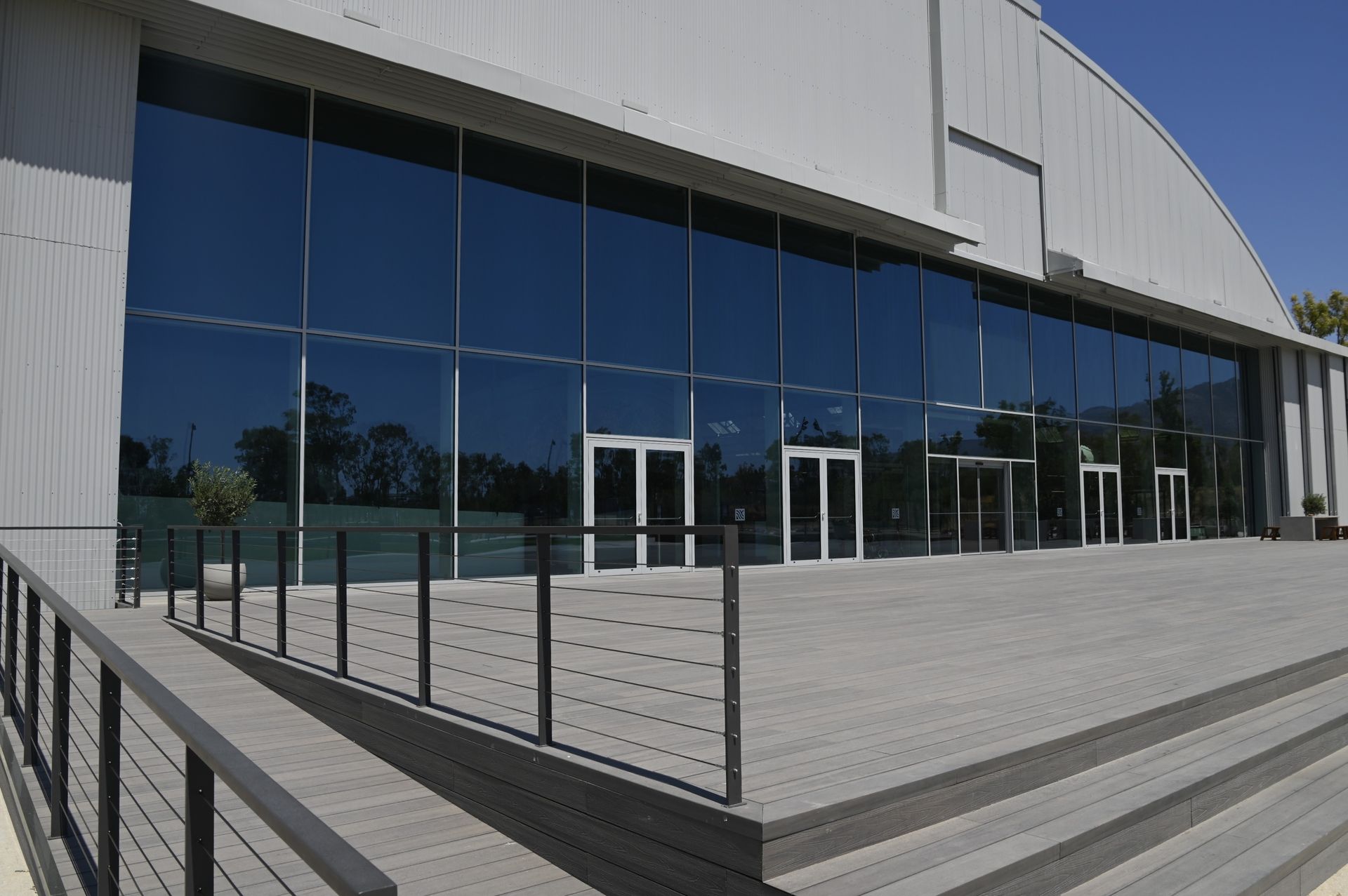 Modern building with large glass windows and multiple entrance doors, gray siding and a gray deck.