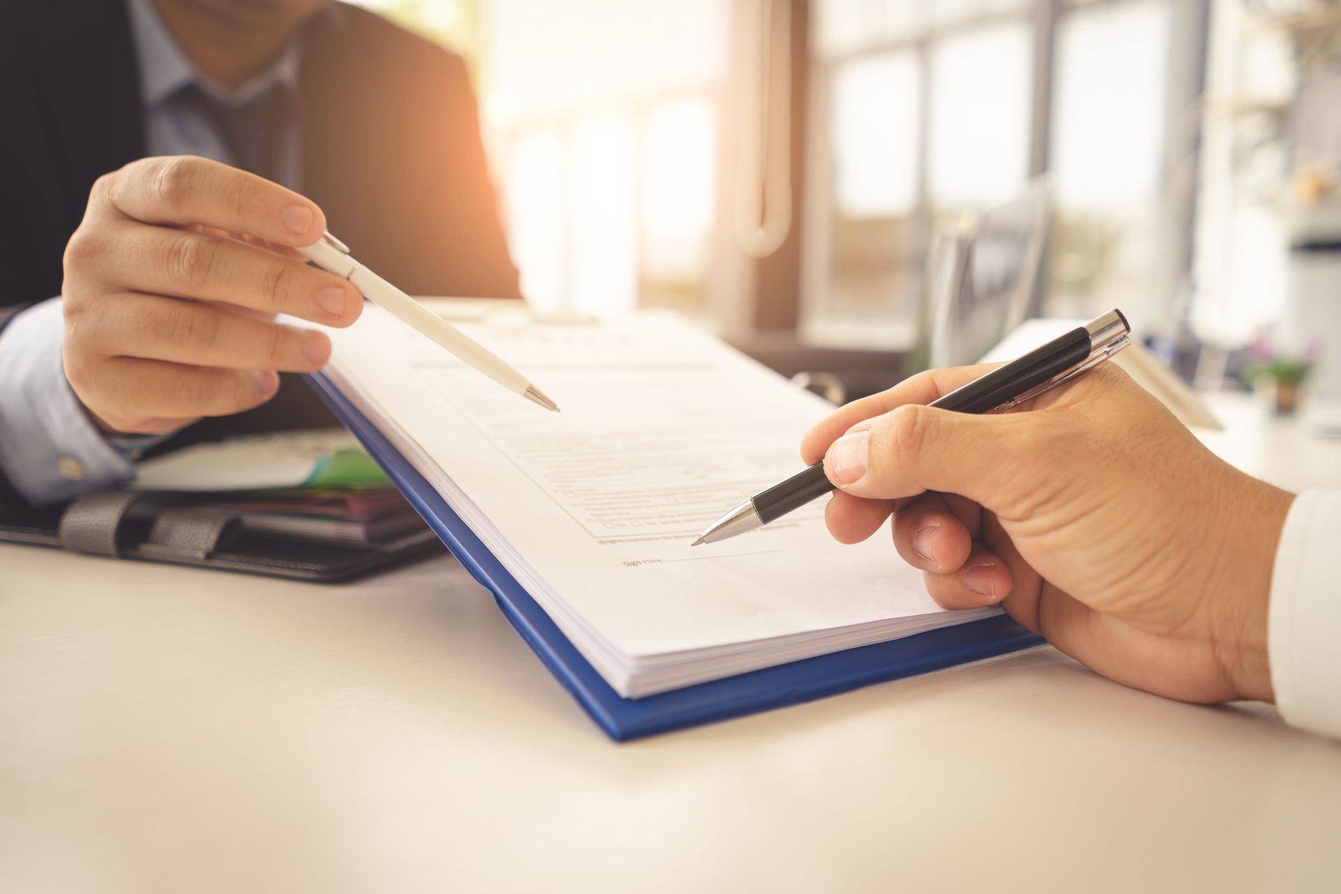 Two people signing a document with pens, close-up shot.