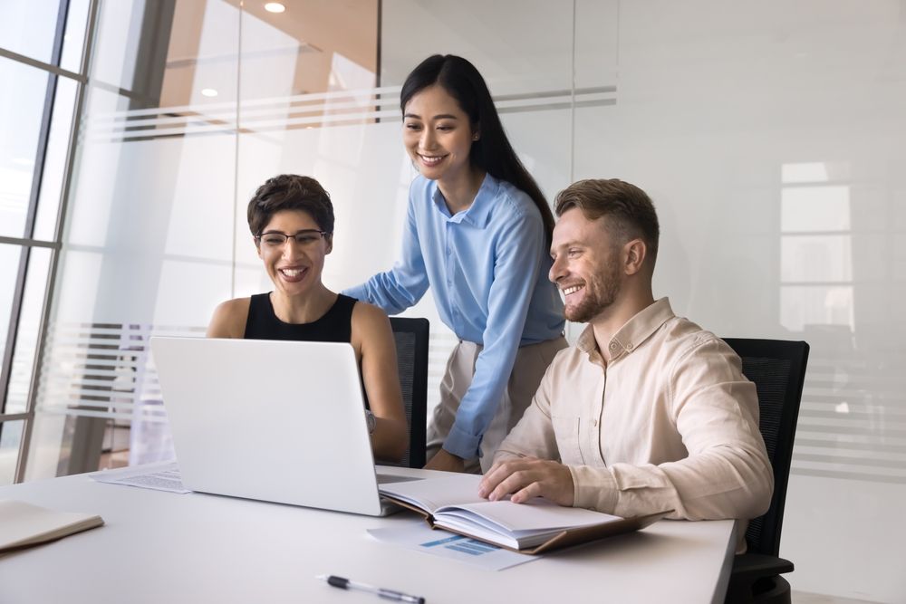 Three professionals smiling while collaborating on a project in a bright, modern office meeting space.