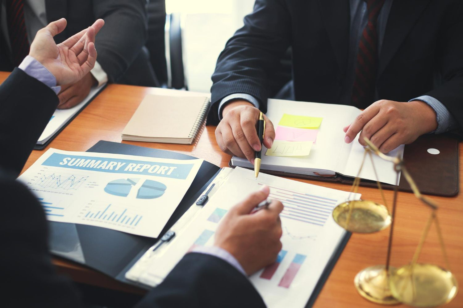 People in suits at a table with papers, charts, and a scale of justice, discussing a report.