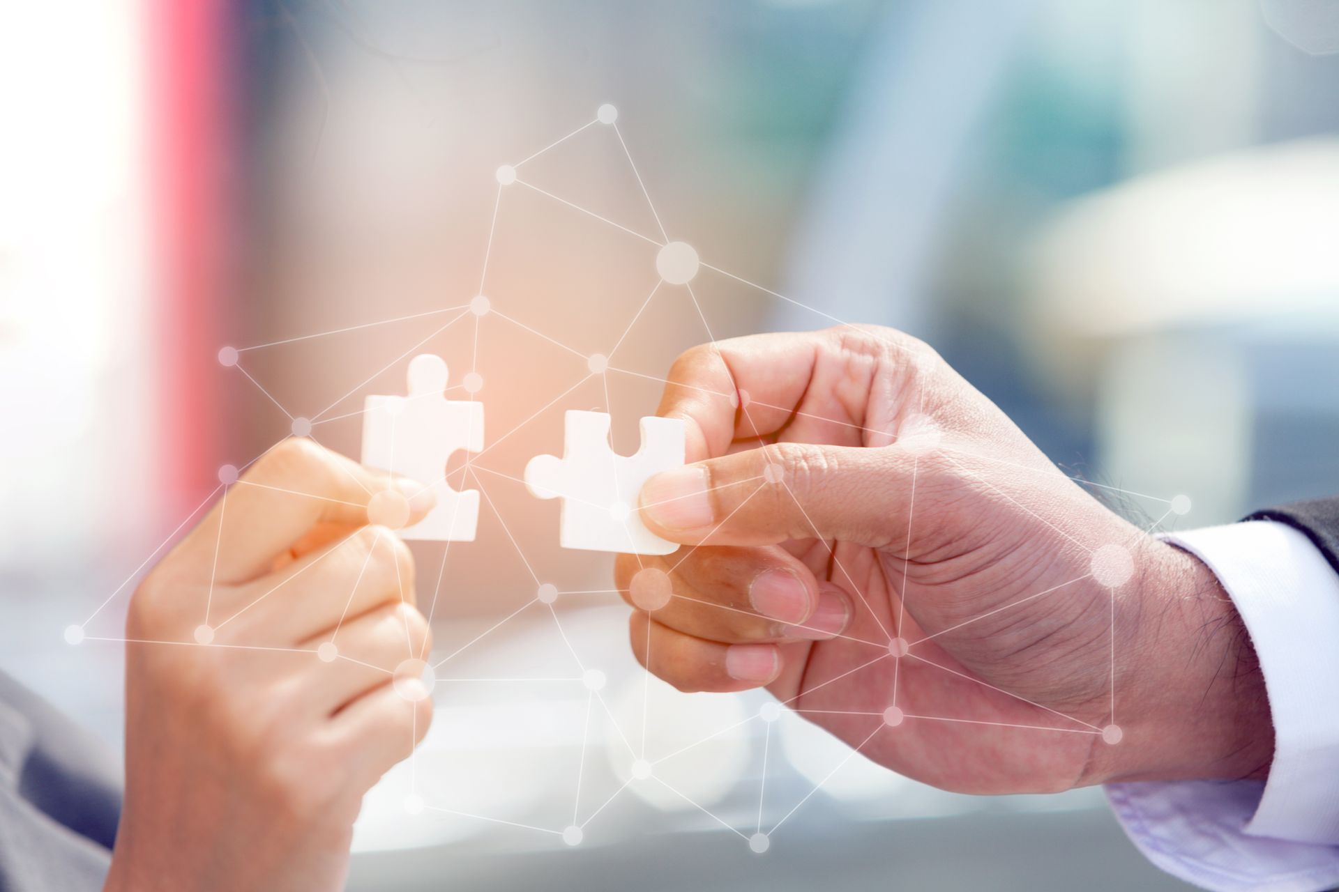 Hands connecting two white puzzle pieces, overlaid with network connections, blurred background.