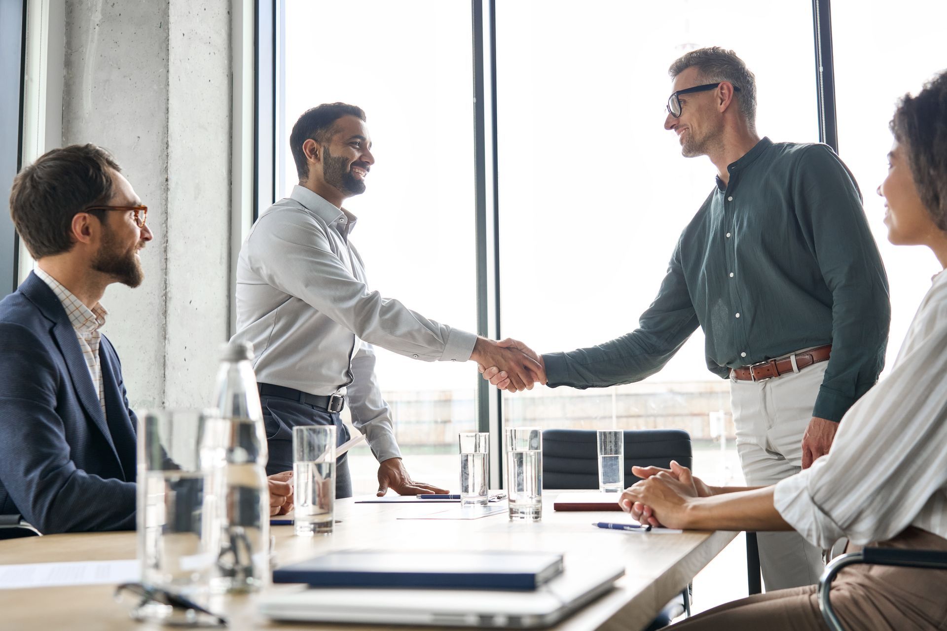 Businesspeople shaking hands in a modern office setting. Two men smiling and gripping hands.