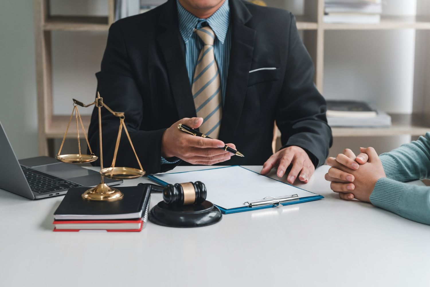 Lawyer explaining paperwork to a client at a desk, scales of justice and gavel present.