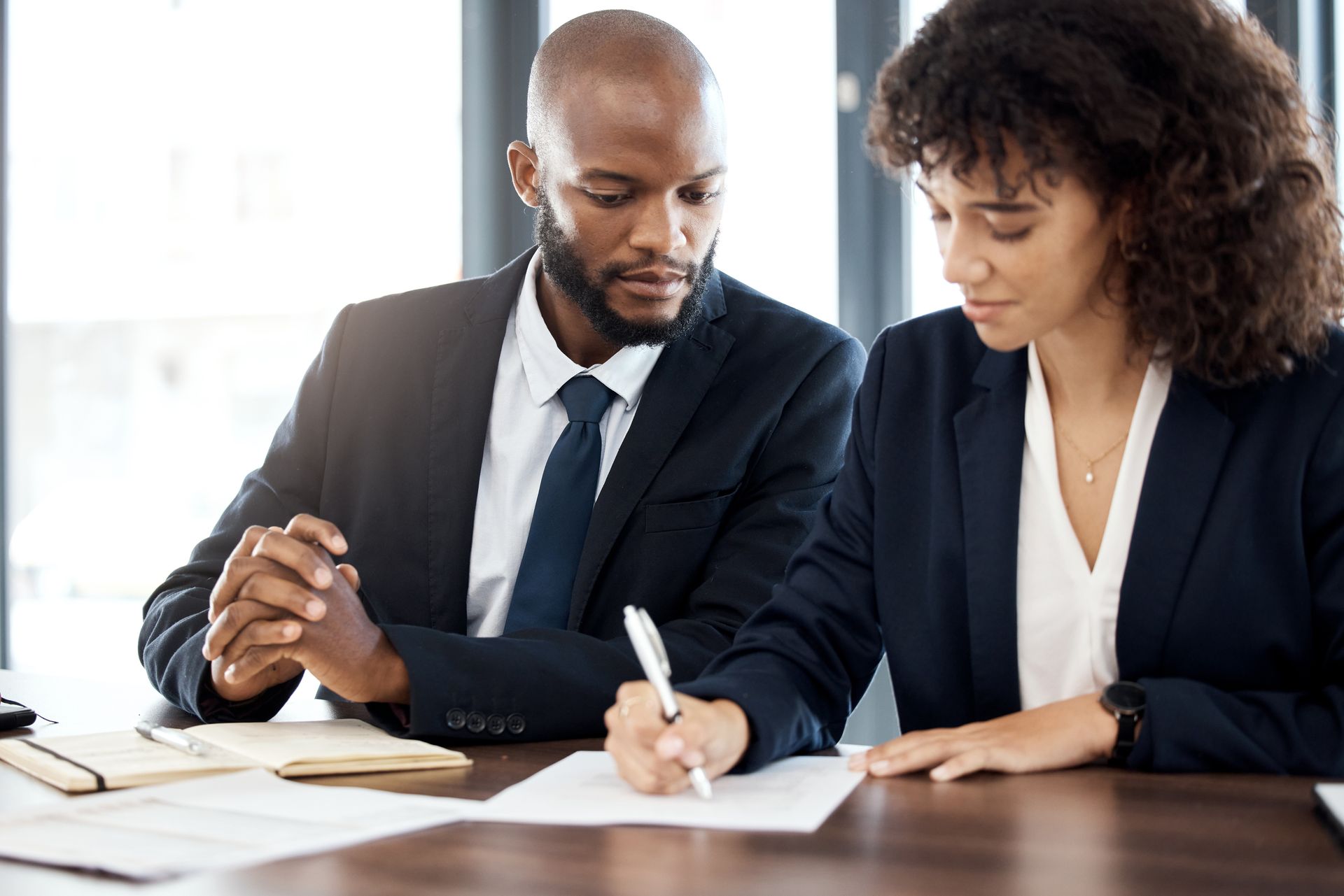 A man and a woman are sitting at a table writing on a piece of paper.