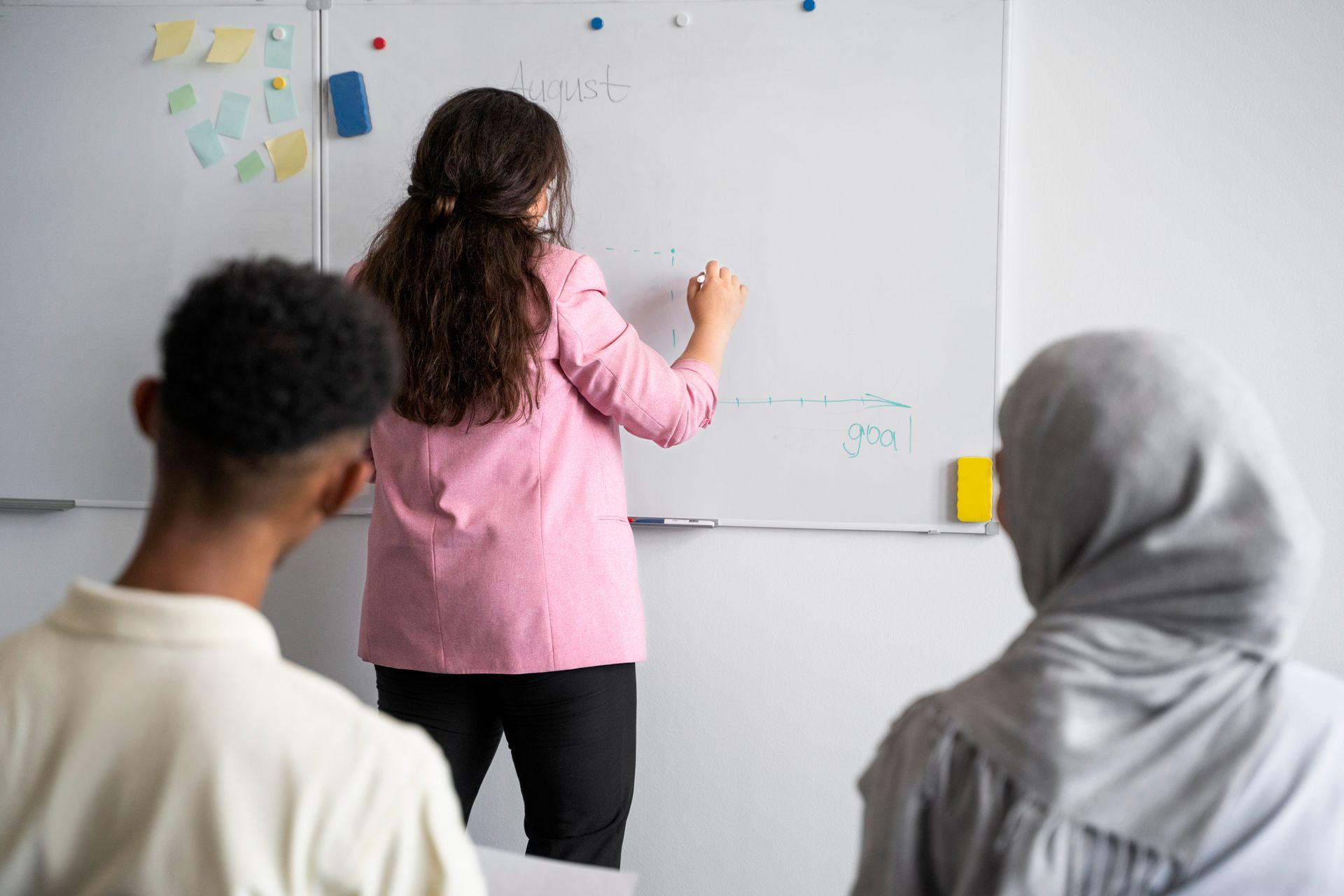 A woman is writing on a whiteboard in front of a group of people.