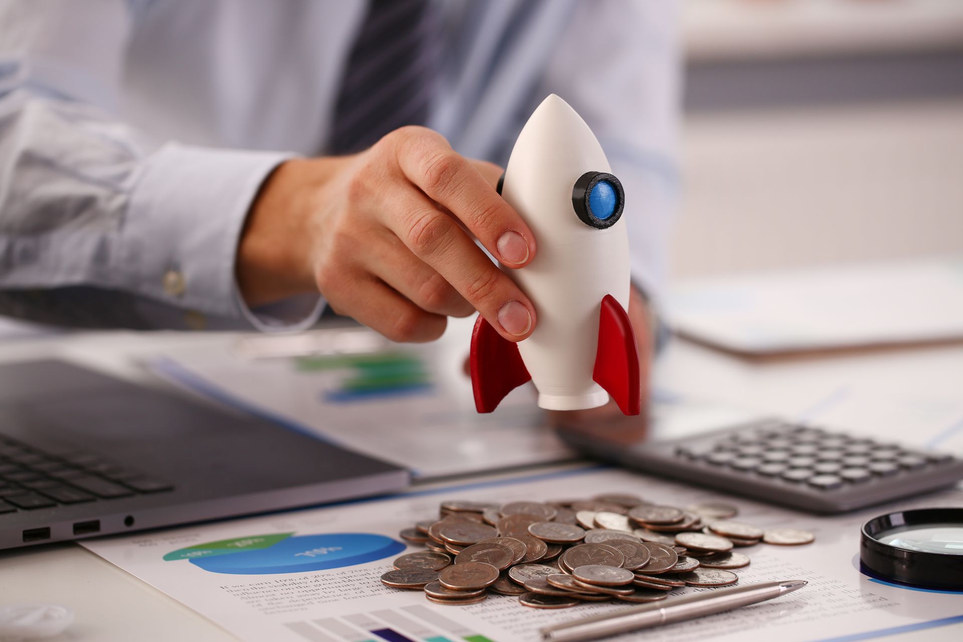 A person is holding a toy rocket over a pile of coins.