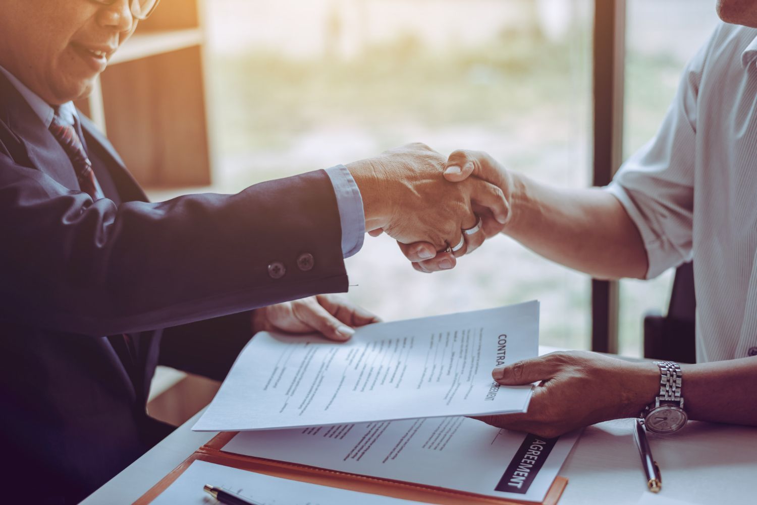 Two men shaking hands over a contract. Sunlight streams in.