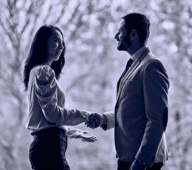 A man and a woman are shaking hands in a park.