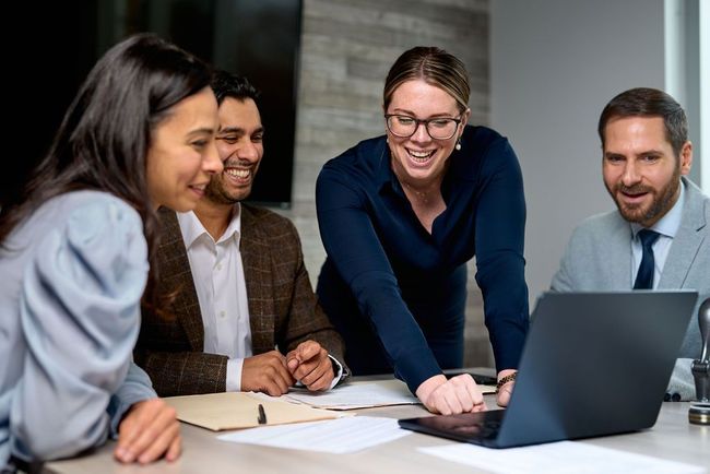 A group of people are sitting around a table looking at a laptop computer.