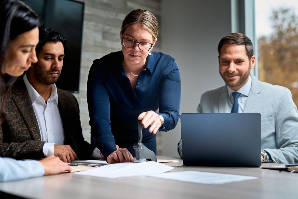 A group of people are sitting around a table looking at a laptop.