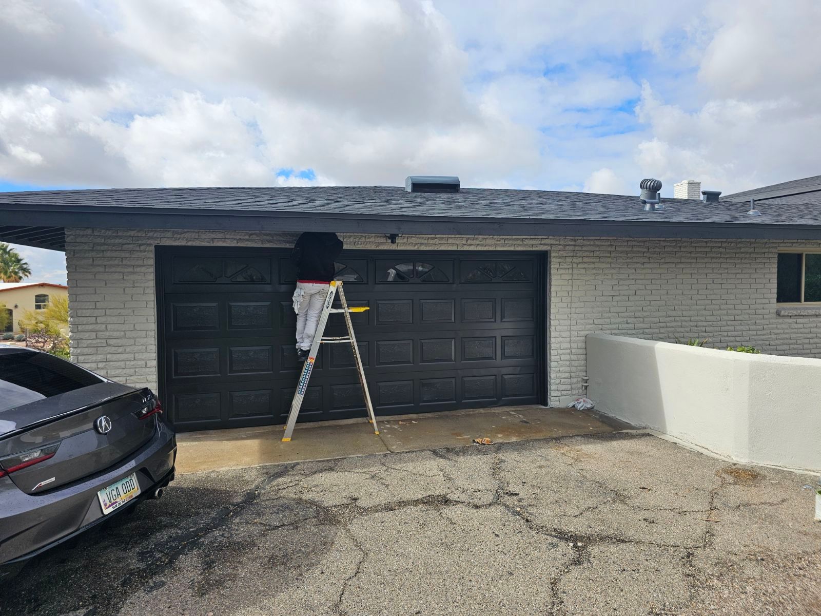 A person is standing on a ladder painting a garage door.
