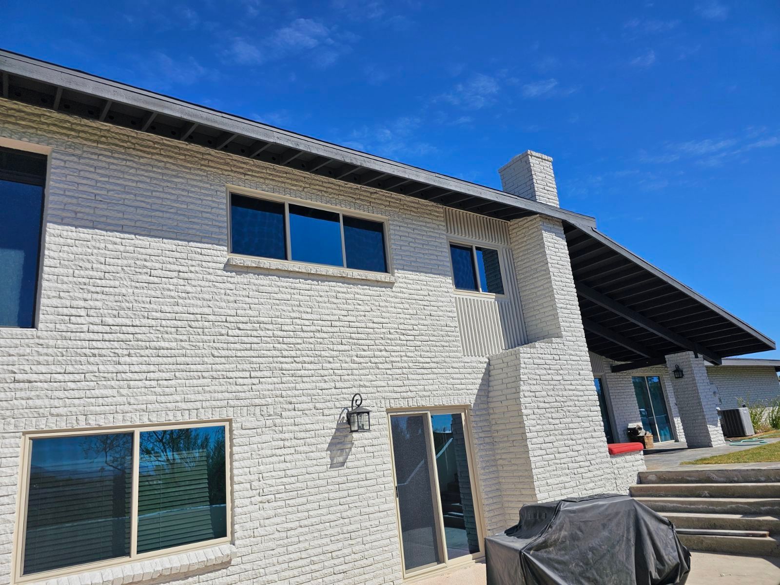 A large white brick house with a bbq in front of it.